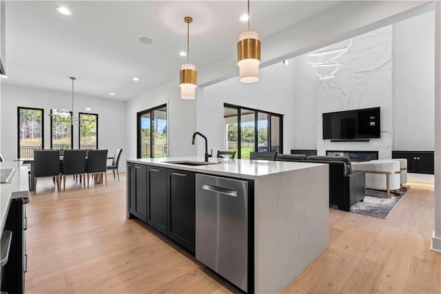 kitchen featuring hanging light fixtures, sink, a kitchen island with sink, dishwasher, and light wood-type flooring