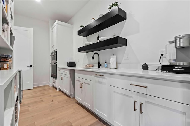 kitchen featuring double oven, light hardwood / wood-style flooring, sink, and white cabinetry