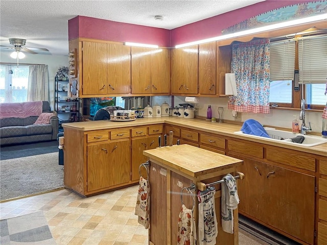 kitchen featuring ceiling fan, sink, a textured ceiling, a center island, and light colored carpet