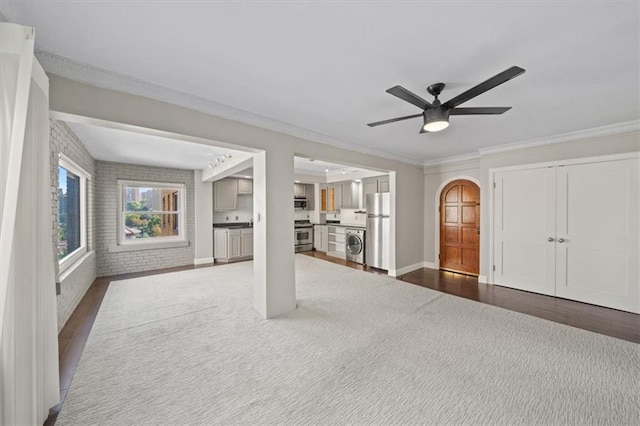 unfurnished living room with brick wall, dark hardwood / wood-style floors, ornamental molding, and ceiling fan