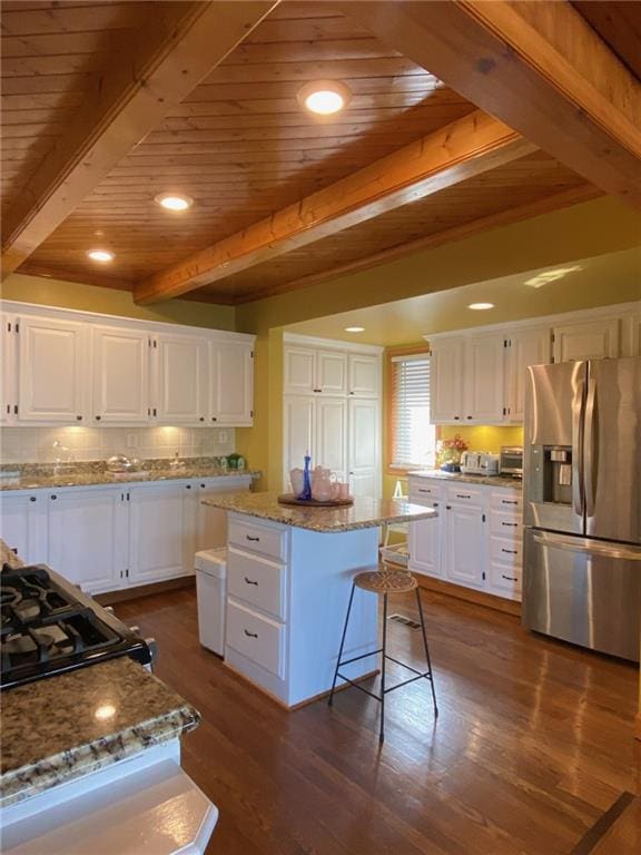 kitchen with dark hardwood / wood-style floors, light stone countertops, white cabinets, a kitchen island, and stainless steel fridge with ice dispenser