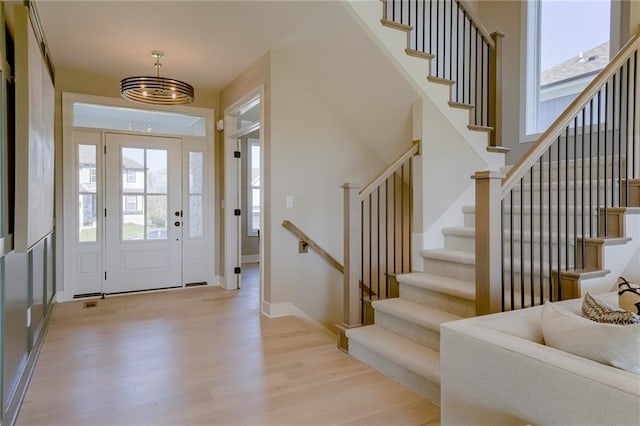 foyer entrance with a healthy amount of sunlight, light hardwood / wood-style flooring, and a notable chandelier