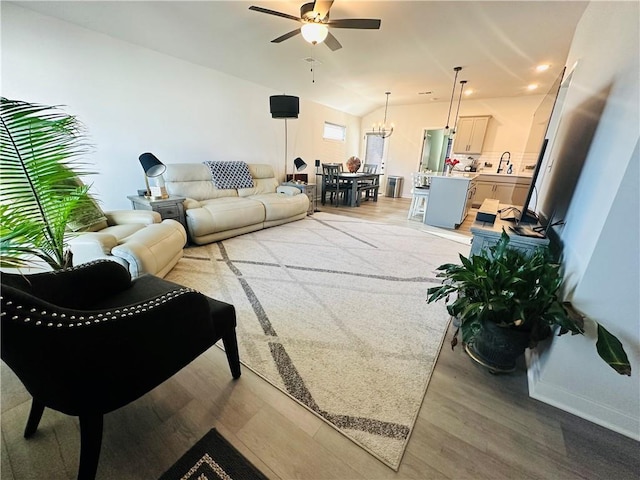 living room with light hardwood / wood-style flooring, lofted ceiling, and ceiling fan with notable chandelier