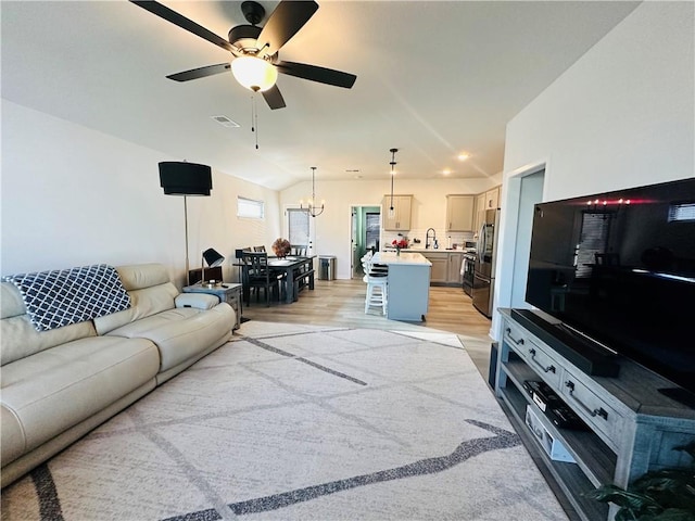 living room with light wood-type flooring, ceiling fan with notable chandelier, vaulted ceiling, and sink