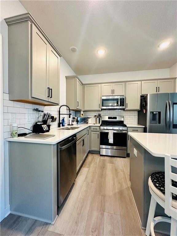 kitchen with gray cabinets, sink, decorative backsplash, light hardwood / wood-style flooring, and appliances with stainless steel finishes