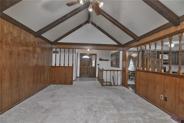 unfurnished living room featuring light carpet, a textured ceiling, wooden walls, and vaulted ceiling with beams