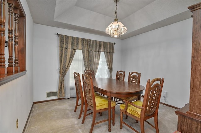 carpeted dining area with a chandelier and a raised ceiling