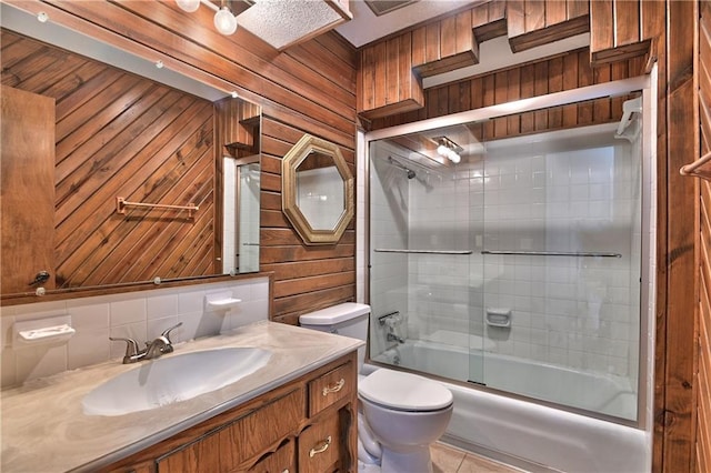 full bathroom featuring toilet, wood walls, bath / shower combo with glass door, and vanity