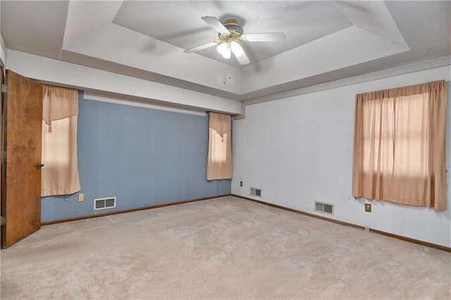 carpeted empty room featuring ceiling fan and a raised ceiling