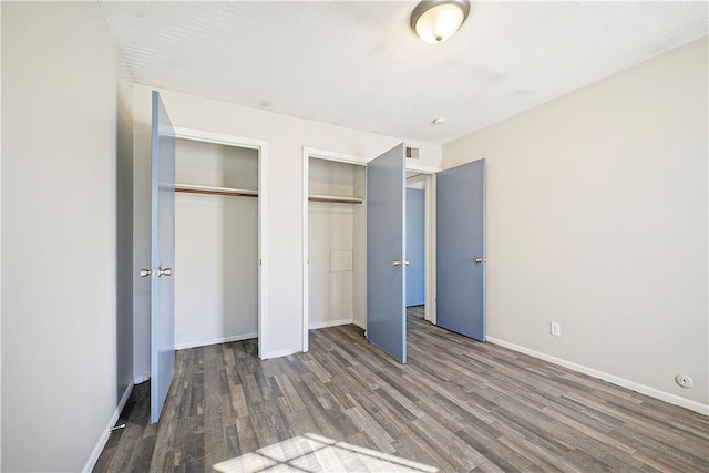 unfurnished bedroom with two closets and dark hardwood / wood-style floors