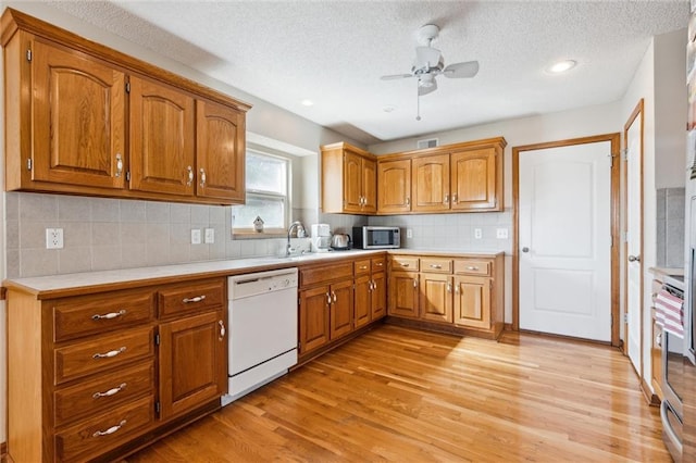 kitchen with white dishwasher, sink, ceiling fan, light wood-type flooring, and a textured ceiling