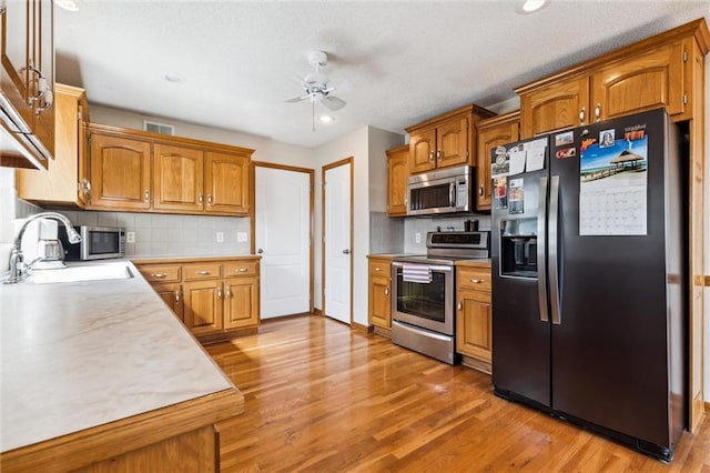 kitchen with appliances with stainless steel finishes, backsplash, ceiling fan, sink, and light hardwood / wood-style flooring