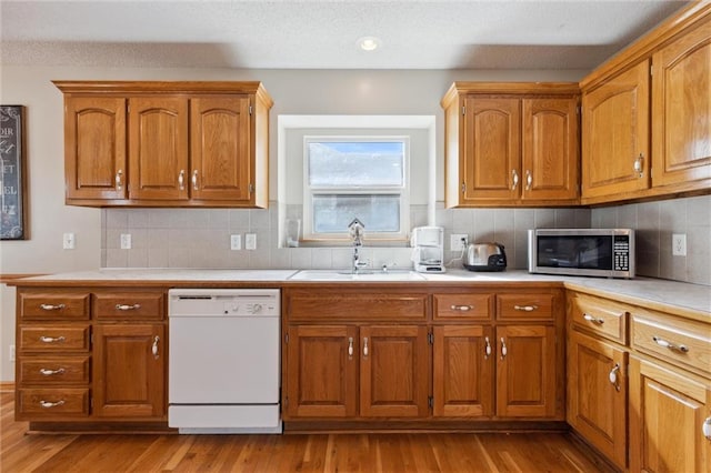 kitchen featuring dishwasher, sink, backsplash, and light hardwood / wood-style flooring