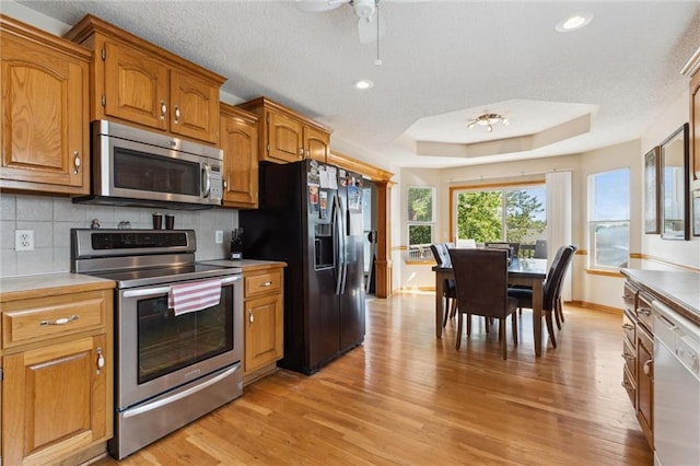 kitchen featuring ceiling fan, tasteful backsplash, appliances with stainless steel finishes, a tray ceiling, and light hardwood / wood-style floors