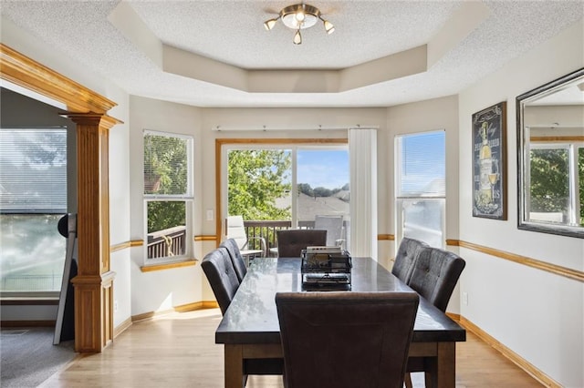 dining room featuring a raised ceiling, ornate columns, and a textured ceiling