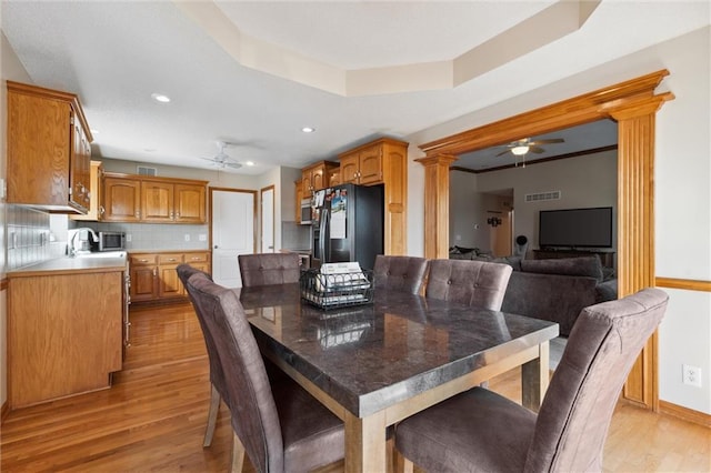 dining space with a raised ceiling, ornate columns, ceiling fan, and light hardwood / wood-style flooring