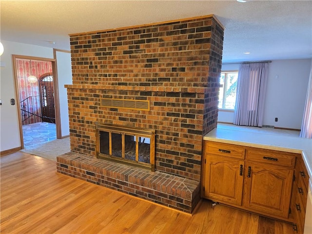 unfurnished living room featuring a brick fireplace, light wood-type flooring, and a textured ceiling