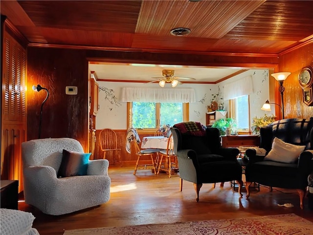 living room with wooden walls, wood-type flooring, wooden ceiling, crown molding, and ceiling fan