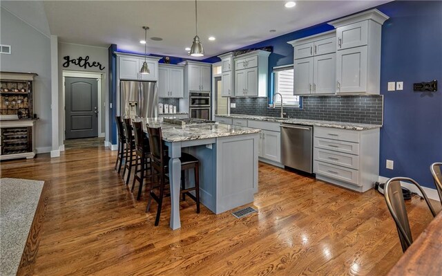 kitchen featuring wood-type flooring, pendant lighting, appliances with stainless steel finishes, and a center island