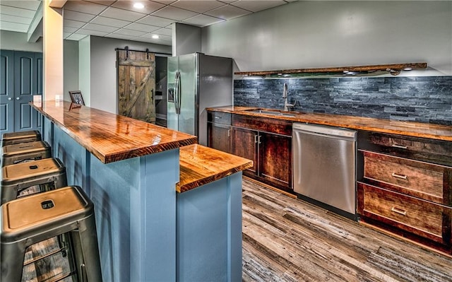 kitchen with sink, stainless steel appliances, a kitchen breakfast bar, a barn door, and wood counters