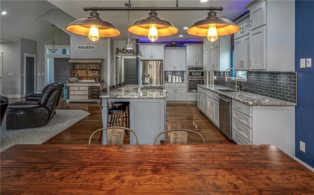 kitchen with pendant lighting, sink, light stone countertops, an island with sink, and appliances with stainless steel finishes