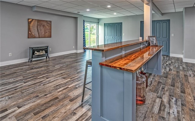 kitchen with a drop ceiling, a breakfast bar area, dark hardwood / wood-style flooring, and a wood stove