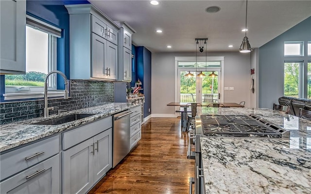 kitchen with appliances with stainless steel finishes, pendant lighting, sink, backsplash, and dark hardwood / wood-style flooring