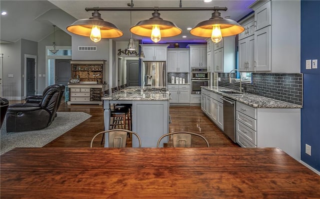 kitchen featuring sink, decorative light fixtures, a center island with sink, stainless steel appliances, and light stone countertops