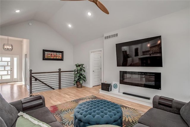 living room with ceiling fan with notable chandelier, wood-type flooring, and vaulted ceiling