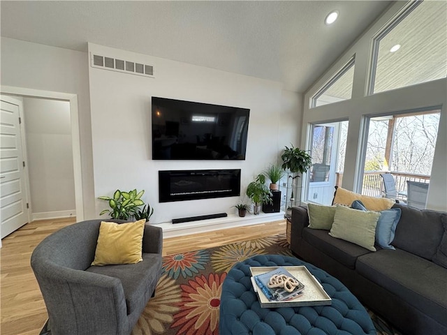 living room featuring a glass covered fireplace, visible vents, recessed lighting, and wood finished floors