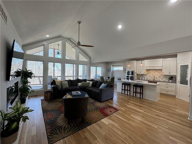 living room featuring visible vents, high vaulted ceiling, plenty of natural light, and light wood-style flooring