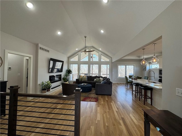 living room featuring light wood finished floors, recessed lighting, visible vents, vaulted ceiling, and baseboards