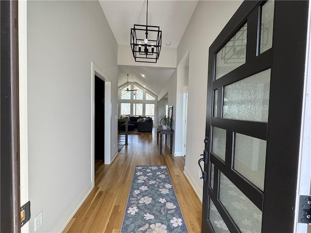 corridor with light wood-type flooring, baseboards, vaulted ceiling, and a notable chandelier