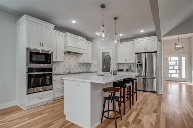 kitchen with light wood finished floors, a breakfast bar, stainless steel appliances, light countertops, and a sink