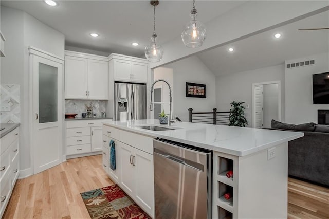 kitchen with light wood finished floors, white cabinets, appliances with stainless steel finishes, open floor plan, and a sink