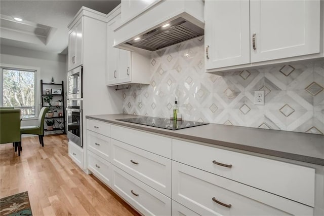 kitchen with oven, black electric cooktop, white cabinetry, custom exhaust hood, and light wood finished floors