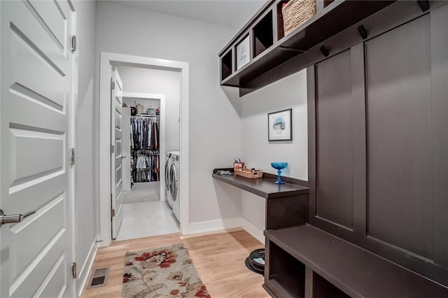 mudroom with built in desk, visible vents, light wood-style floors, washer and dryer, and baseboards