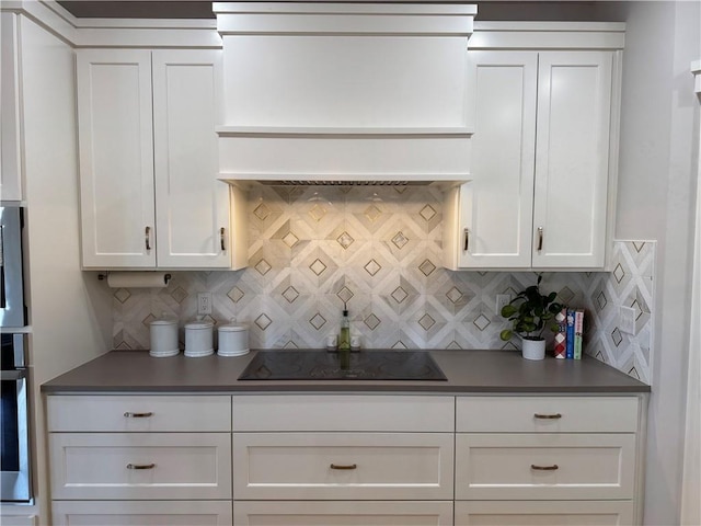 kitchen with custom exhaust hood, dark countertops, white cabinetry, and black electric stovetop