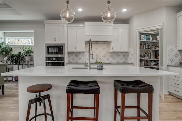 kitchen with built in microwave, a center island with sink, white cabinets, light wood-type flooring, and oven