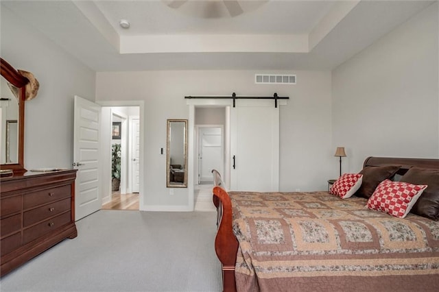 carpeted bedroom featuring a barn door, a raised ceiling, visible vents, and a ceiling fan