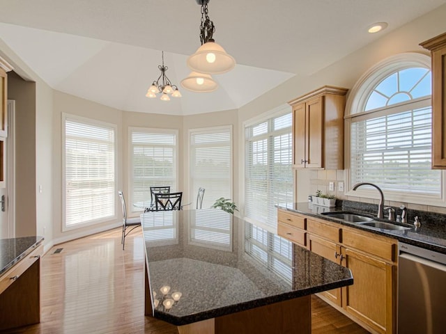 kitchen with decorative light fixtures, sink, dark stone countertops, a center island, and stainless steel dishwasher