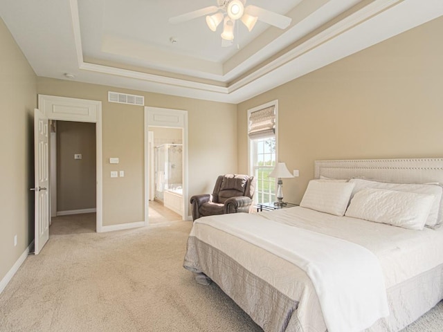 bedroom with a raised ceiling, connected bathroom, light colored carpet, and ceiling fan