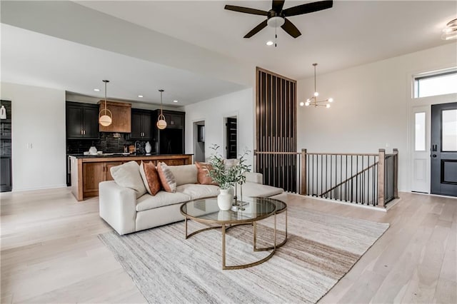 living room featuring ceiling fan with notable chandelier and light wood-type flooring