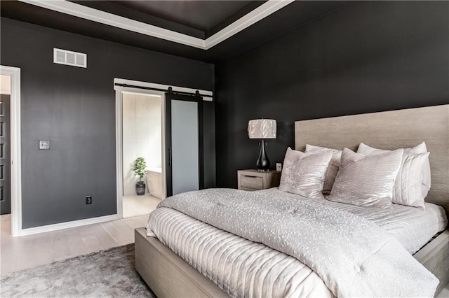 bedroom with ensuite bathroom, a barn door, and wood-type flooring