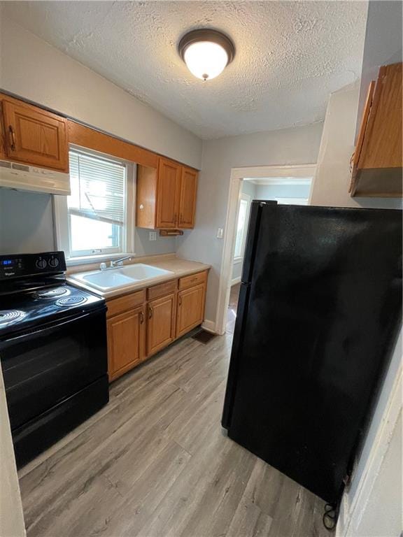 kitchen with a textured ceiling, light hardwood / wood-style flooring, sink, and black appliances