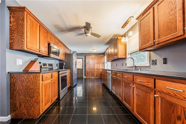 kitchen with ceiling fan, stainless steel appliances, dark tile patterned flooring, sink, and hanging light fixtures