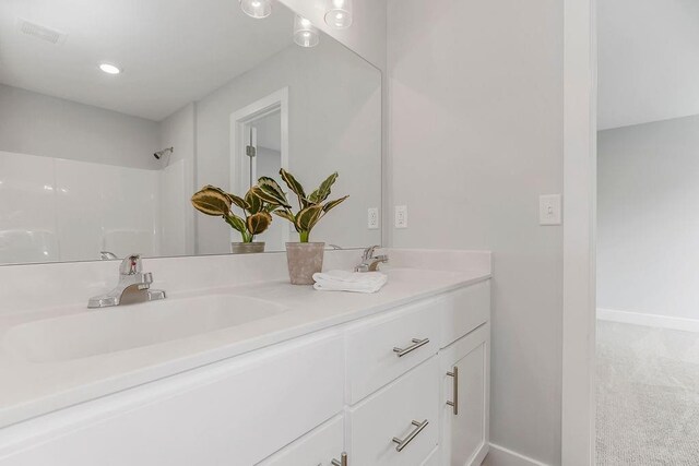 bathroom with double vanity, walk in shower, visible vents, and a sink