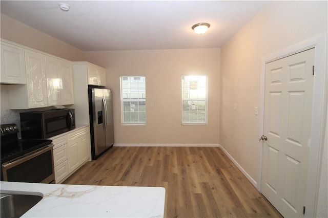 kitchen with light stone counters, white cabinetry, appliances with stainless steel finishes, and light hardwood / wood-style flooring