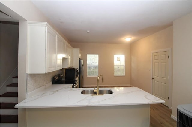 kitchen with light stone counters, sink, white cabinets, hardwood / wood-style floors, and black range with electric stovetop