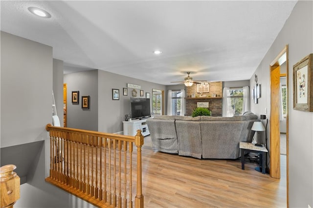 living room featuring wood-type flooring, a brick fireplace, and ceiling fan